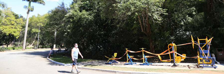Pessoa caminha no Parque Aclimação, com máscara, ao lado de árvores grandes e folhagens verdes